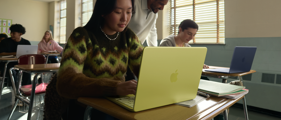 Eine Schülerin verwendet ein MacBook Neo in der Farbe Zitrus, das nicht am Strom angeschlossen ist, in einem Klassenzimmer